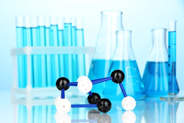 Molekülmodell und Reagenzgläser mit Flüssigkeit auf blauem Hintergrund — Stockfoto