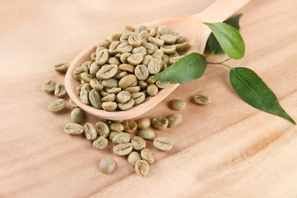 Granos de café verdes en cuchara y hojas sobre fondo de madera — Foto de Stock