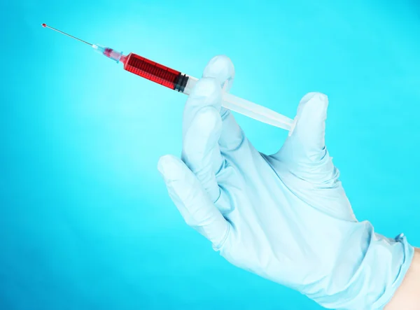 Hand holding syringe filled with blood on blue background — Stock Photo, Image