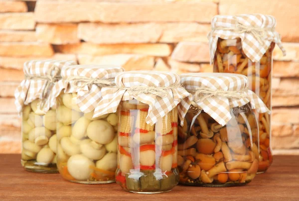 Delicious marinated mushrooms in glass jars, on wooden table on bright background — Stock Photo, Image