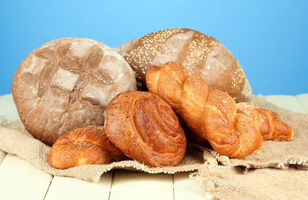 Sammansättning med bröd, rullar på säckväv, på träbord, på färgbakgrund — Stockfoto
