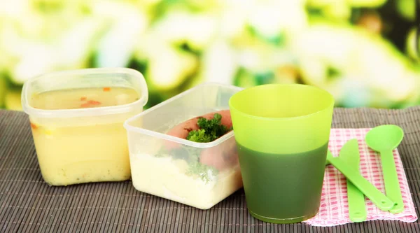 Tasty lunch in plastic containers, on bamboo mat on bright background — Stock Photo, Image