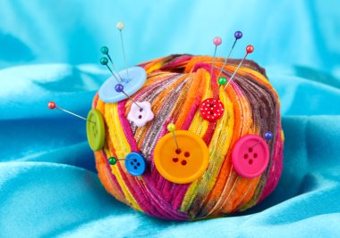 Colorful buttons and multicolor wool ball on color fabric background