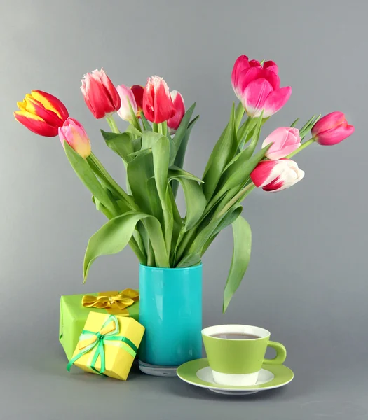 Piękne tulipany w wiaderku z darów i filiżankę herbaty na szarym tle — Zdjęcie stockowe