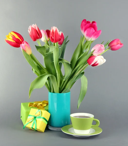 Belles tulipes dans un seau avec des cadeaux et une tasse de thé sur fond gris — Photo