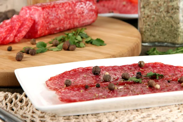 Välsmakande salami på plattan och styrelsen på träbord närbild — Stockfoto