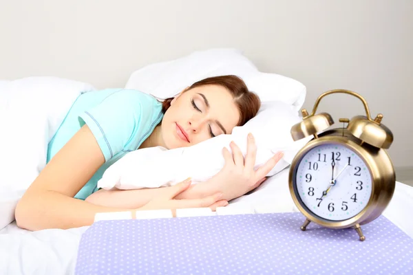 Beautiful young woman sleeping on bed with alarm clock in bedroom — Stock Photo, Image