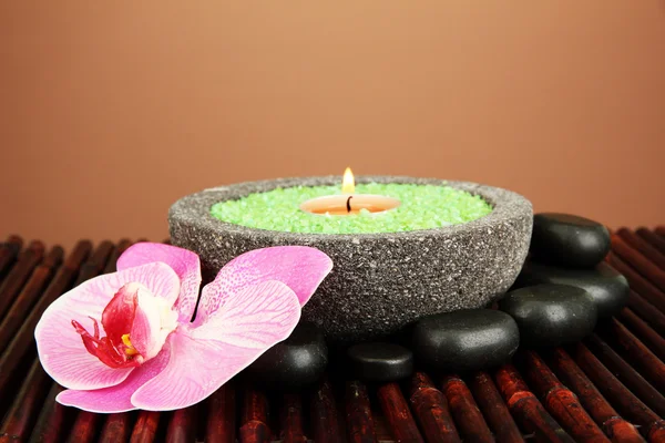 Candle in stone bowl with marine salt, on bamboo mat, on brown background — Stock Photo, Image