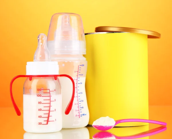 Botellas con leche y alimentos para bebés sobre fondo naranja — Foto de Stock