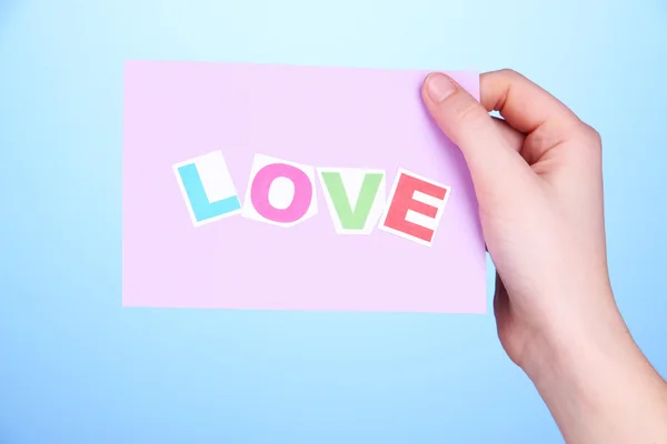 Palabra de amor sobre papel trozo en mano sobre fondo azul —  Fotos de Stock