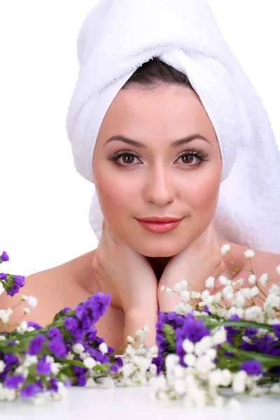 Mooie jonge vrouw met handdoek op haar hoofd en bloemen geïsoleerd op wit — Stockfoto