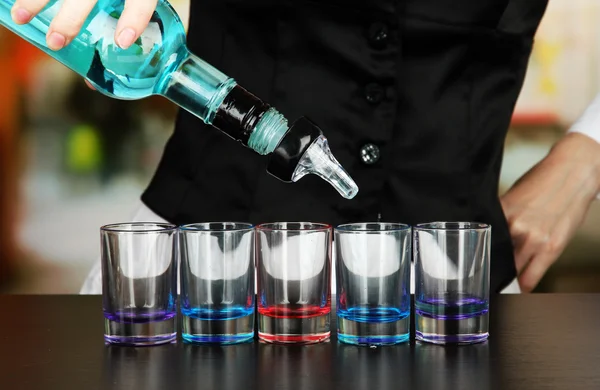 Barmen hand with bottle pouring beverage into glasses, on bright background — Stock Photo, Image