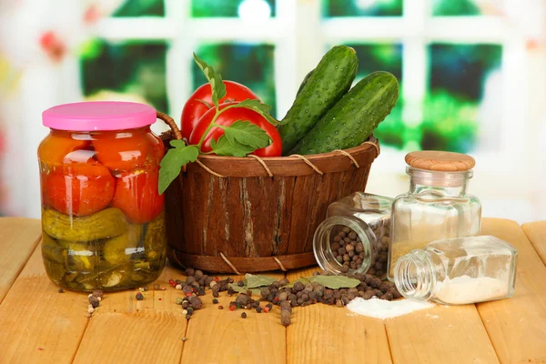 Tasty green cucumbers and red tomatoes in basket, on wooden table on bright background — Stock Photo, Image