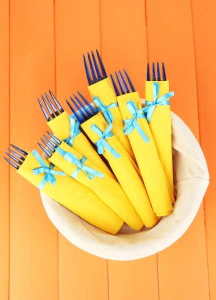 裹在黄色纸餐巾，在篮子里，彩色木制背景上的蓝色塑料叉子 — 图库照片