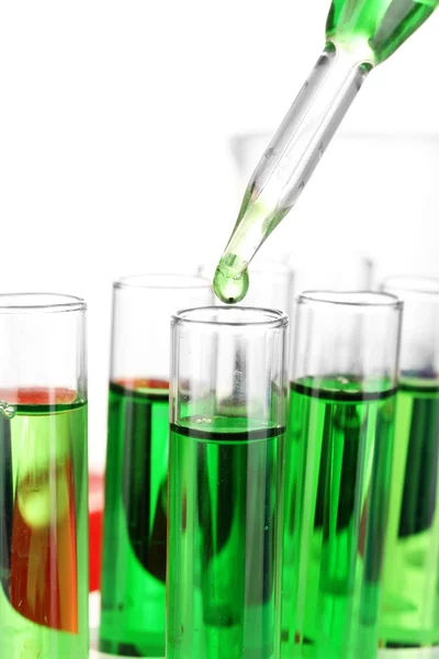 Pipeta de laboratório com gota de líquido de cor sobre tubos de ensaio de vidro, de perto, isolado em branco — Fotografia de Stock