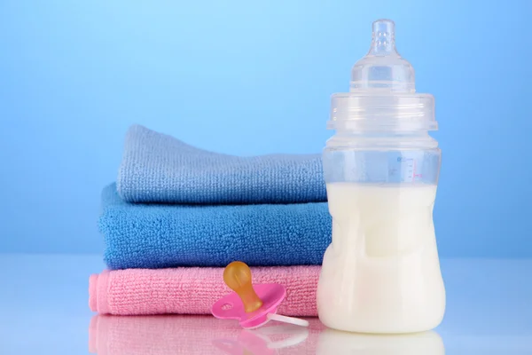 Bottle for milk with towels and nipple on blue background — Stock Photo, Image