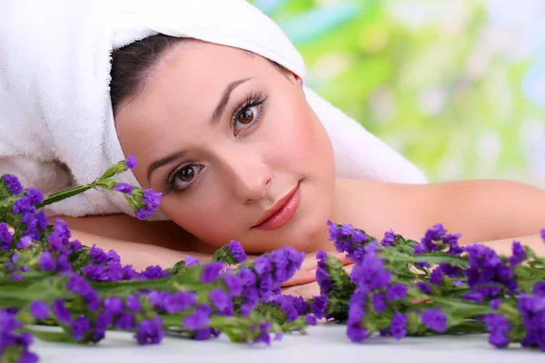 Hermosa joven con toalla en la cabeza y flores sobre fondo brillante —  Fotos de Stock