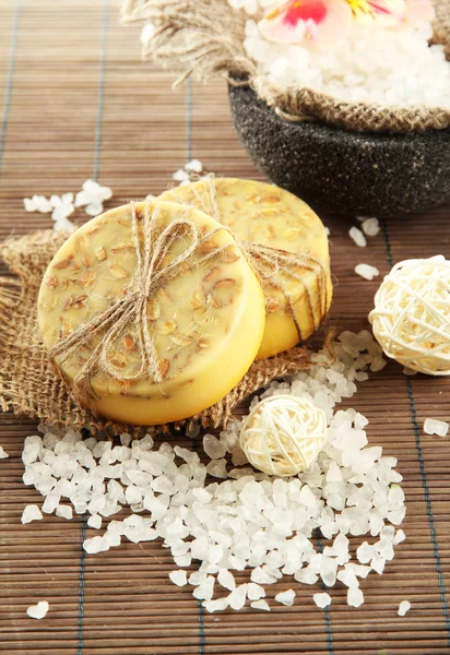 Hand-made soap and sea salt on grey bamboo mat — Stock Photo, Image