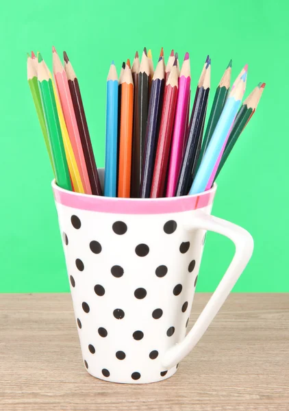 Kleurrijke potloden in cup op tabel op groene achtergrond — Stockfoto