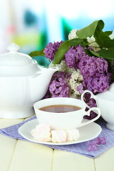 Sammansättning med vackra lila blommor, te service på träbord på ljus bakgrund — Stockfoto