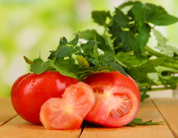 Fresh tomatoes and young plant on wooden table on natural background — Stock Photo, Image