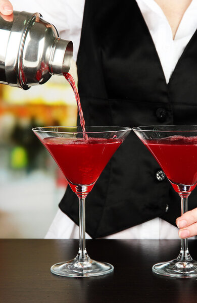 Barmen hand with shaker pouring cocktail into glasses, on bright background
