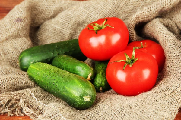 Вкусные зеленые огурцы и красные помидоры на фоне мешковины — стоковое фото