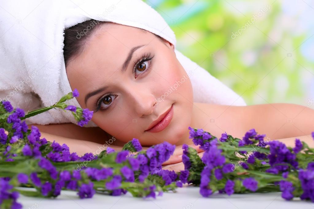 Beautiful young woman with towel on her head and flowers on bright background