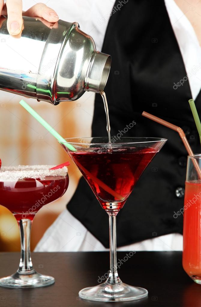 Barmen hand with shaker pouring cocktail into glass, on bright background