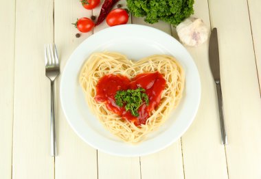 Cooked spaghetti carefully arranged in heart shape and topped with tomato sauce, on wooden background