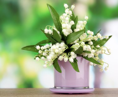 Beautiful lily of the valley in vase on nature background clipart