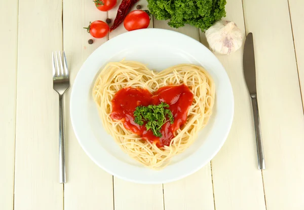 Esparguete cozido cuidadosamente dispostos em forma de coração e coberto com molho de tomate, no fundo de madeira — Fotografia de Stock
