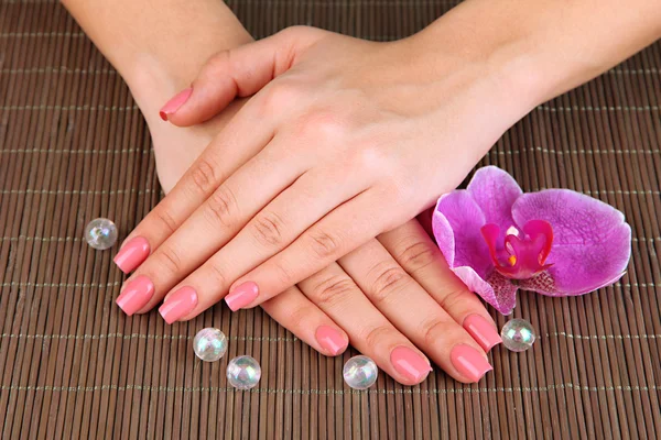 Frauenhände mit rosa Maniküre und Orchidee auf Bambusmatte Hintergrund — Stockfoto