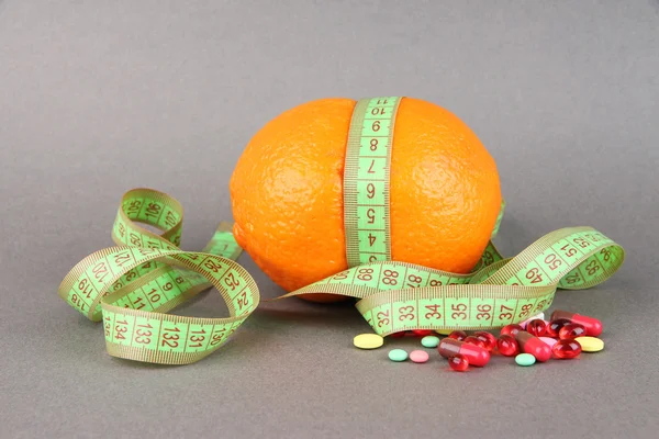 Orange with measuring tape and multicolor pills, on color background — Stock Photo, Image