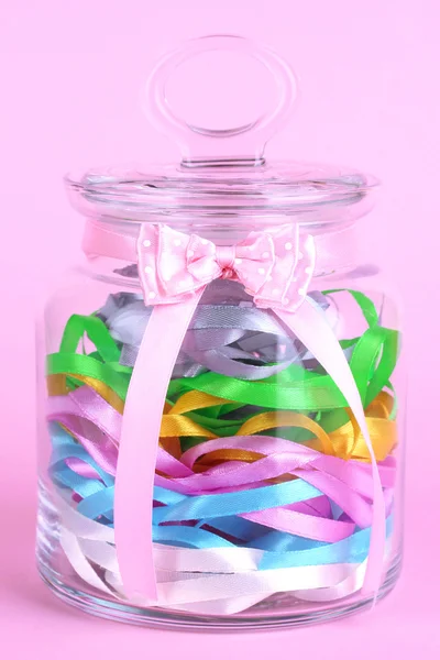 Glass jar containing various colored ribbons on pink background — Stock Photo, Image
