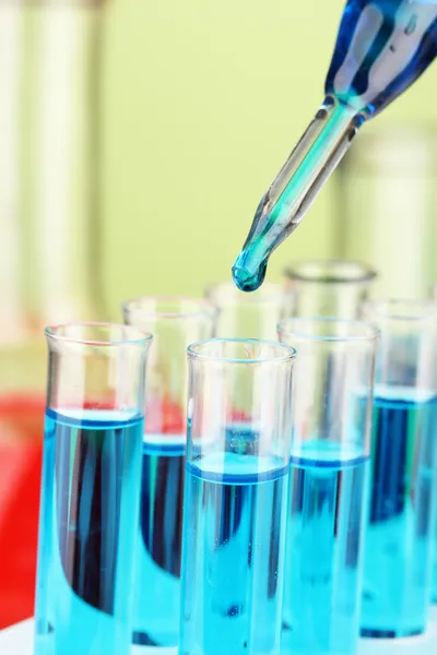 Pipeta de laboratorio con gota de líquido de color sobre tubos de ensayo de vidrio, primer plano —  Fotos de Stock