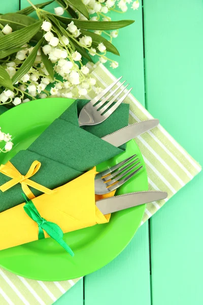 Tenedores y cuchillos envueltos en servilletas de papel verde y amarillo, sobre fondo de madera de color —  Fotos de Stock