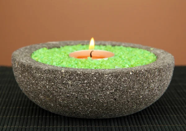 Свеча в каменной чаше с морской солью, на бамбуковом коврике, на коричневом фоне — стоковое фото