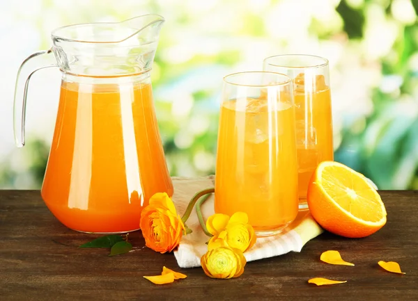 Vasos y jarra de zumo de naranja sobre mesa de madera, sobre fondo verde — Foto de Stock