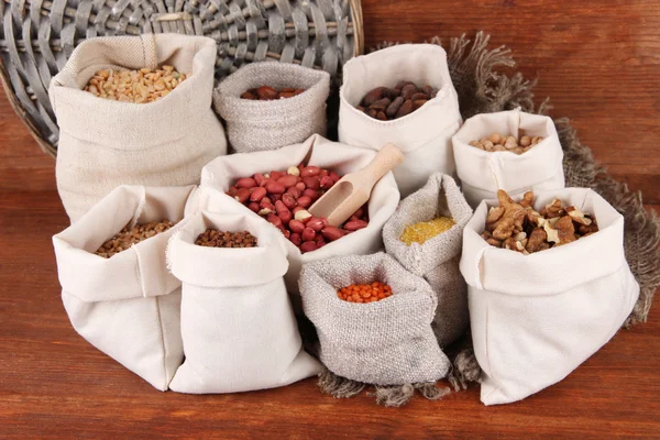 Diversi tipi di fagioli in sacchi su sfondo di legno — Foto Stock