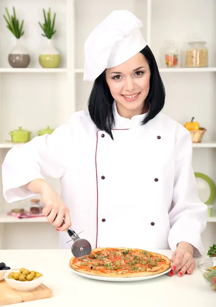 Mooi meisje chef-fornuis met pizza op keuken achtergrond — Stockfoto