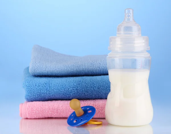 Flasche für Milch mit Handtüchern und Brustwarzen auf blauem Hintergrund — Stockfoto