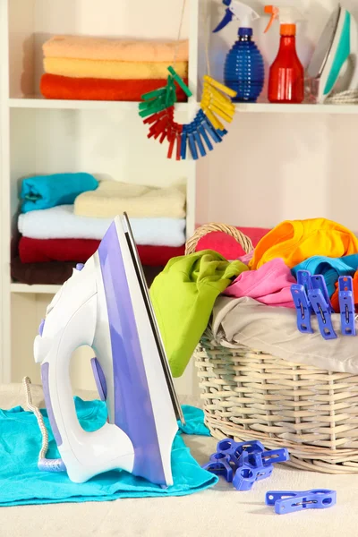 Ropa y plancha en la mesa sobre los estantes de fondo — Foto de Stock