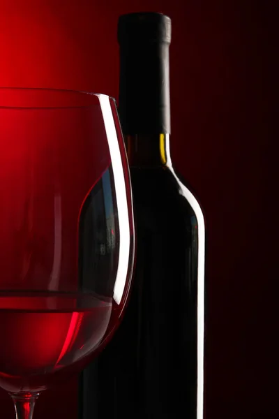 Sklenka vína s lahví na zářivě červeném pozadí — Stock fotografie