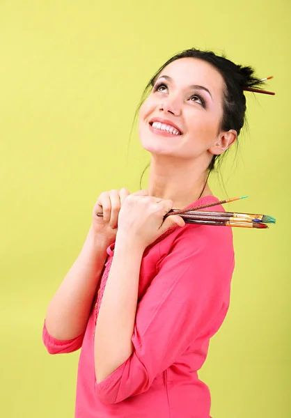 Krásná mladá žena malíř s kartáči na barvu pozadí — Stock fotografie