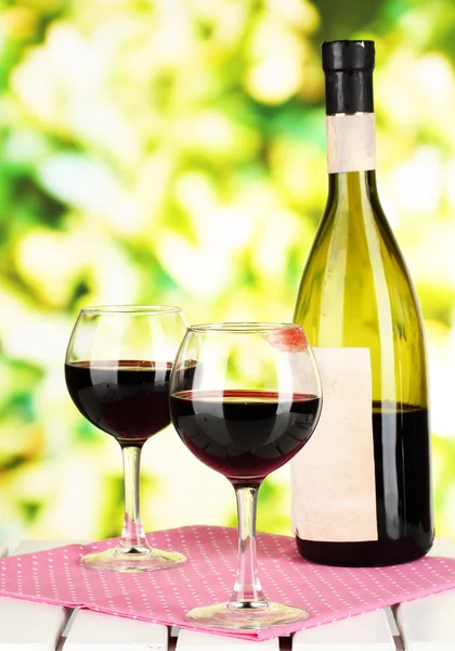 Two glasses of wine and bottle on table on nature background — Stock Photo, Image