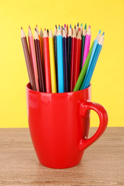Lápis coloridos na xícara na mesa no fundo amarelo — Fotografia de Stock