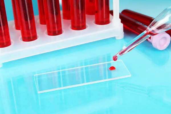 Tubos de ensaio com sangue em laboratório sobre fundo azul — Fotografia de Stock