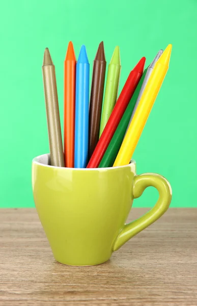 Lápis coloridos na xícara na mesa sobre fundo verde — Fotografia de Stock