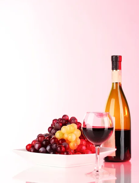 Copo de vinho com marca de batom, uvas e garrafa sobre fundo rosa — Fotografia de Stock